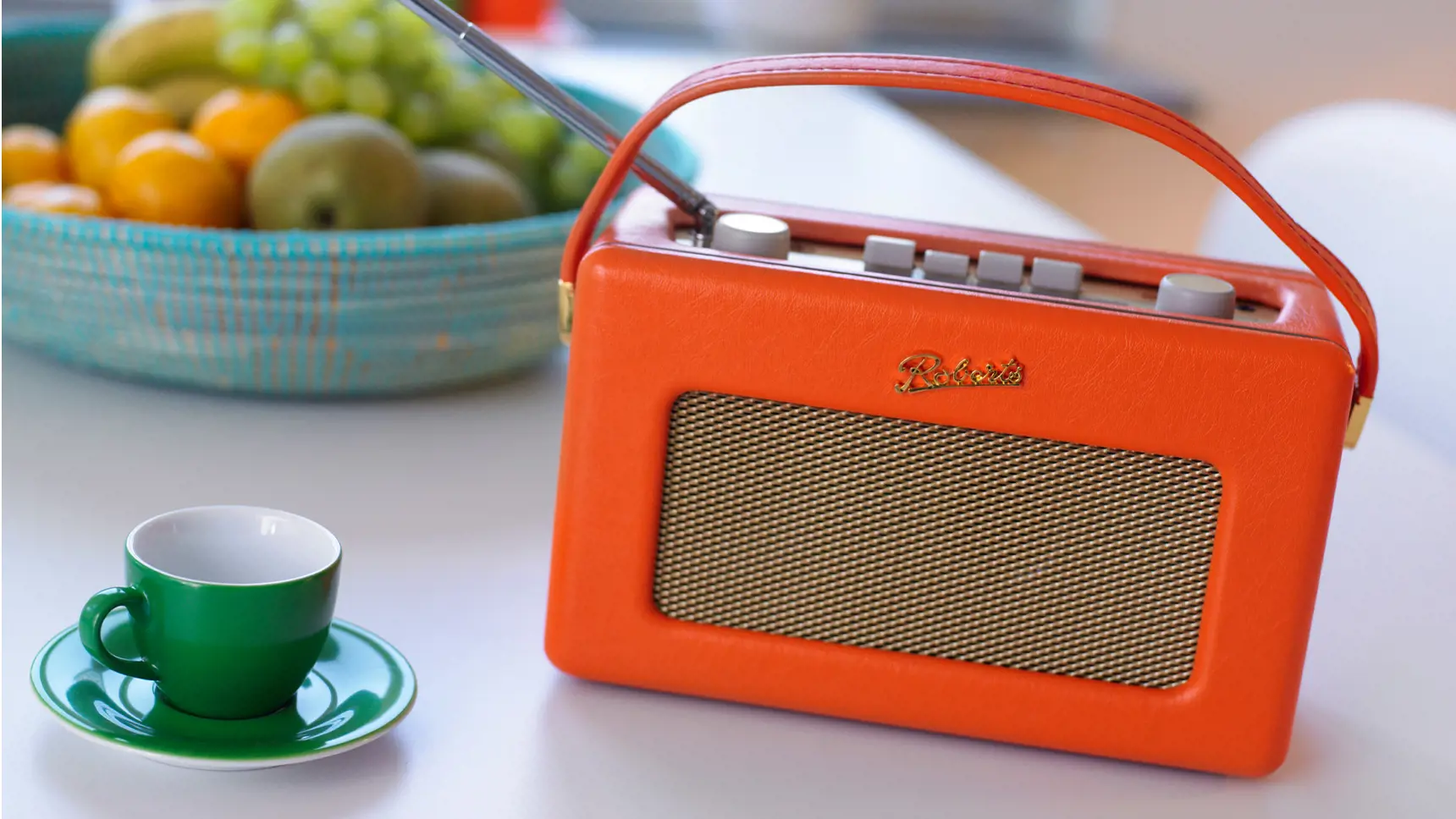 Gammal batteriradio på ett bord. Bredvid står en kaffekopp och en fruktskål.